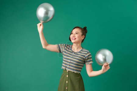 Photo for Happy smiling woman is looking on an air silver balloon having fun over a green background. - Royalty Free Image