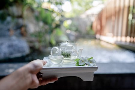 Photo for "Hand holding the tray served transparent teapot with herbal tea." - Royalty Free Image