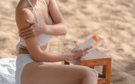 Téléchargez les photos : Woman on the beach applying Sunscreen while sitting on towel. - en image libre de droit