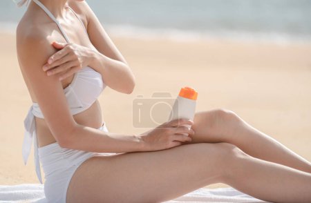 Téléchargez les photos : Woman on the beach applying Sunscreen while sitting on towel. - en image libre de droit