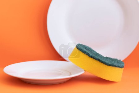 Foto de Esponja amarilla junto a plato blanco con fondo naranja - Imagen libre de derechos