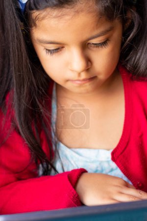 Téléchargez les photos : Little girl sitting playing with her tablet at home - en image libre de droit