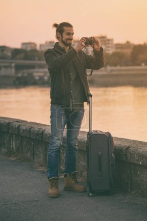 Téléchargez les photos : Homme d'affaires avec valise photographiant ville - en image libre de droit