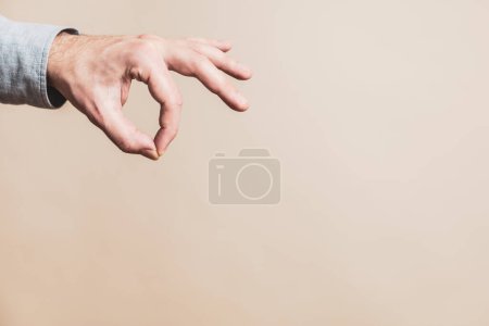 Téléchargez les photos : Male hand in picking gesture on beige background - en image libre de droit