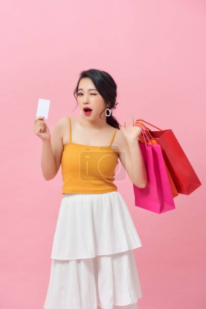 Foto de Full length portrait of a happy beautiful girl wearing dress and holding shopping bags and showing credit card isolated over pink background - Imagen libre de derechos