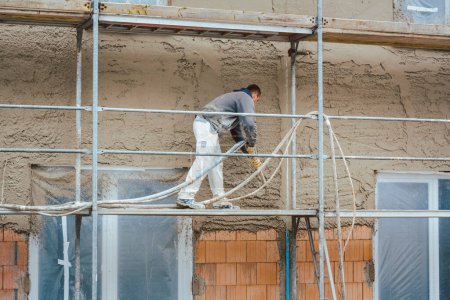 Téléchargez les photos : Ouvrier plâtrage mur extérieur de la maison nouvellement construite - en image libre de droit