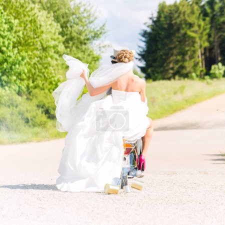 Photo for "Bridal pair driving motor scooter wearing gown and suit" - Royalty Free Image