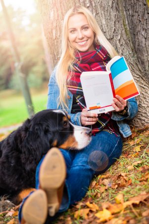 Foto de "Mujer con libro de lectura de perros en el parque de otoño
" - Imagen libre de derechos