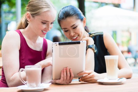 Téléchargez les photos : Deux jeunes femmes meilleures amies utilisant une tablette PC à l'extérieur dans un endroit branché du centre-ville - en image libre de droit