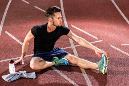 Photo for "Athlete stretching on racing track before running" - Royalty Free Image