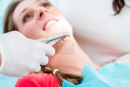 Photo for "Dentist extracting tooth of woman with extractor" - Royalty Free Image