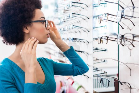 Foto de "Mujer negra probándose las gafas en la tienda de óptica
" - Imagen libre de derechos