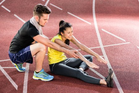 Photo for "Man and woman on cinder track of sports arena stretching exercises" - Royalty Free Image