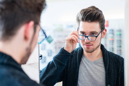 Photo for "Man testing glasses in optician shop mirror" - Royalty Free Image