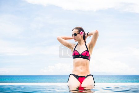 Photo for "Woman sitting at the edge of infinity pool in hotel resort" - Royalty Free Image