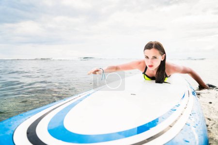 Photo for "Girl surfer paddling on surfboard to the open sea" - Royalty Free Image