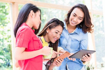 Téléchargez les photos : Trois jeunes femmes s'amusent en regardant une tablette PC pendant la pause au travail - en image libre de droit