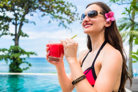 Photo for "Tourist woman in red bikini drinking cocktail at beach " - Royalty Free Image