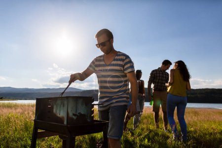 Téléchargez les photos : Cercle d'amis ayant barbecue dans le champ près de la mer - en image libre de droit