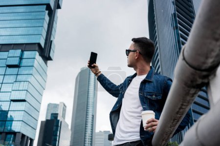 Téléchargez les photos : "Jeune homme prenant des photos selfie dans un quartier d'affaires moderne de Jakarta" - en image libre de droit