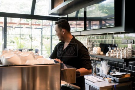 Foto de "Joven trabajando como camarero detrás del mostrador de la barra de una cafetería limpia y moderna " - Imagen libre de derechos
