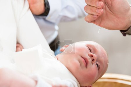 Foto de Bebé está llorando en el bautizo mientras el sacerdote vierte agua bendita - Imagen libre de derechos