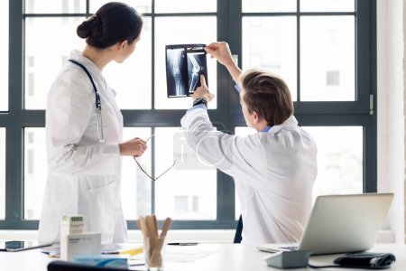 Photo for "Experienced orthopedist helping his colleague with the interpretation of an X-ray in the office" - Royalty Free Image