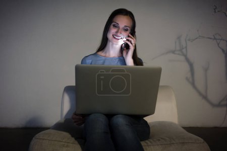 Téléchargez les photos : Jeune pigiste avec smartphone et ordinateur portable en chambre noire le soir - en image libre de droit