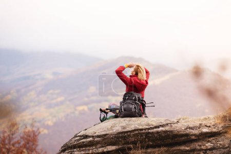 Photo for "Hiker girl taking a rest on a rock in the mountains. Windy day. Travel and healthy lifestyle outdoors in fall season" - Royalty Free Image