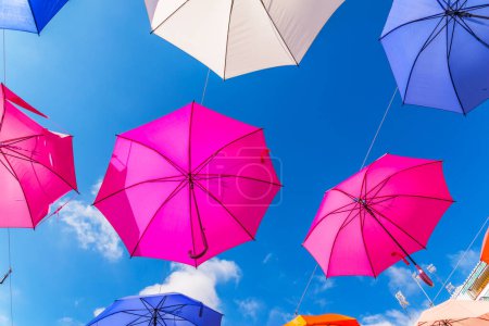 Foto de "Colourful umbrellas urban street decoration. Hanging colorful umbrellas over blue sky, tourist attraction" - Imagen libre de derechos