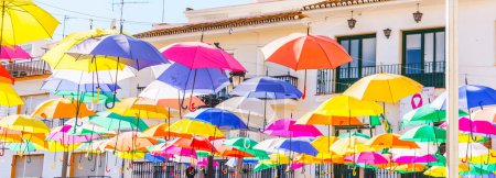 Foto de "Colourful umbrellas urban street decoration. Hanging colorful umbrellas over blue sky, tourist attraction" - Imagen libre de derechos