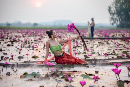 Téléchargez les photos : "Les jeunes femmes asiatiques en robe traditionnelle dans le bateau et les fleurs de lotus rose dans l'étang.Belles filles en costume traditionnel.Thaïe. Ayutthaya, élégance." - en image libre de droit