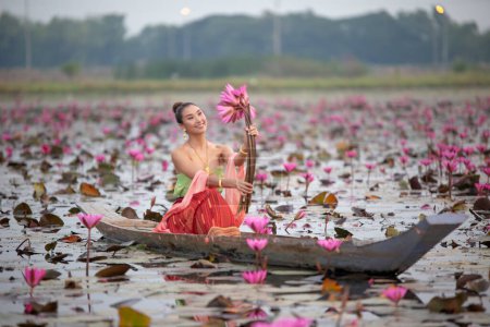 Téléchargez les photos : "Les jeunes femmes asiatiques en robe traditionnelle dans le bateau et les fleurs de lotus rose dans l'étang.Belles filles en costume traditionnel.Thaïe. Ayutthaya, élégance." - en image libre de droit