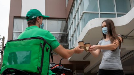 Photo for "Young man delivering food to customer at doorway, Paper pocket and food containers in hands of a smiling deliveryman outdoors. Quality service of a restaurant." - Royalty Free Image