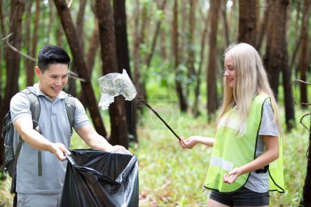 Téléchargez les photos : "Volontariat vert. Optimiste deux bénévoles tenant un sac poubelle et aidant à ramasser les ordures au parc, ils ramassent les ordures et les mettent dans un sac poubelle noir. concept de protection écologique." - en image libre de droit