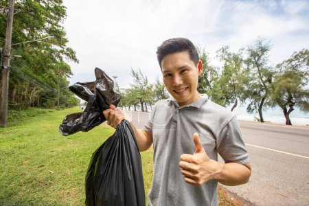 Photo for "Green volunteering. Optimistic two volunteers holding garbage bag and help picking up trash at park, they're picking up the garbage and putting it in a black garbage bag. ecology protection concept." - Royalty Free Image