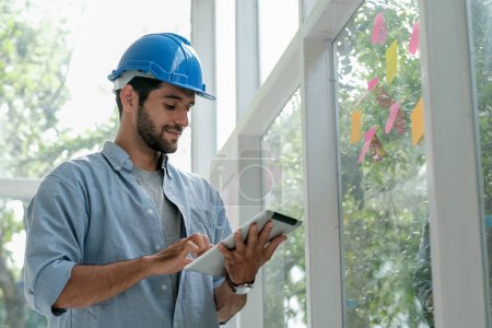 Photo for "Caucasian engineer work in office with glass windows and use tablet to manage system also contact with other co-worker." - Royalty Free Image