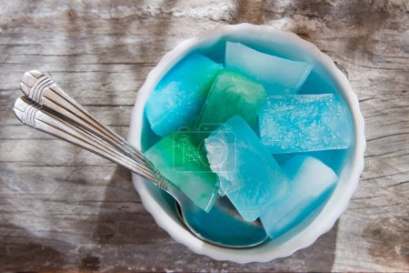 Photo for Bowl of colored ice-cubes on wooden table - Royalty Free Image