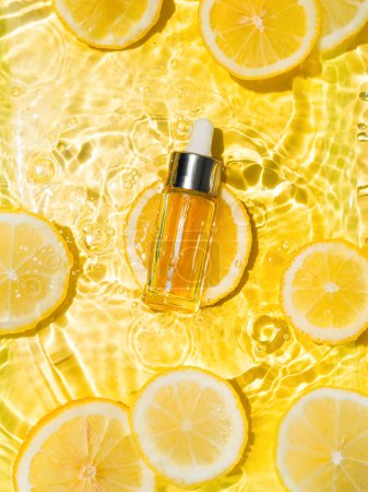 Foto de Botella cosmética en agua, rodajas de limón, fondo amarillo - Imagen libre de derechos