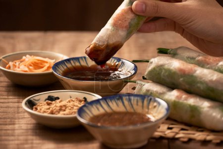Photo for "Hand dipping vegetarian rice paper rolls into the soy sauce" - Royalty Free Image