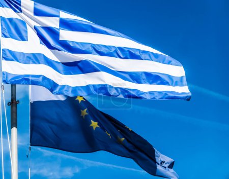 Foto de "Flags of Greece and European Union on blue sky background, politics of Europe" - Imagen libre de derechos