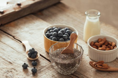 Photo for "Fresh blueberries, almond and chia seeds with milk on wooden board. Ideal healthy breakfast concept. " - Royalty Free Image