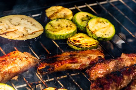Téléchargez les photos : "Griller les rouleaux de viande appelés mici ou mititei avec des légumes sur le barbecue de l'omble. Grill au charbon avec feu brûlant" - en image libre de droit