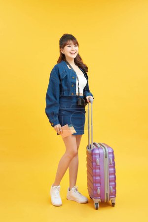 Foto de Concepto de viaje. mujer feliz chica con maleta y pasaporte sobre fondo de color amarillo - Imagen libre de derechos