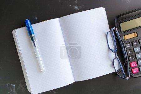 Téléchargez les photos : Top view Blank Notebook Calculator and glasses on a black marble table background. - en image libre de droit