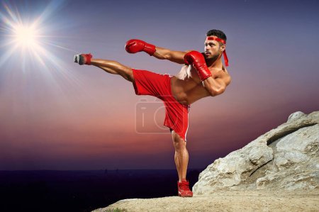 Photo for Boxer in training on the hillside at sunset, evening workouts, side kick, red boxing gloves, red boxing form, man with a naked torso, muscles, developed muscles, muscular body, athlete. - Royalty Free Image