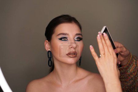 Téléchargez les photos : Maquilleuse prenant une photo mobile pour le modèle avec maquillage - en image libre de droit