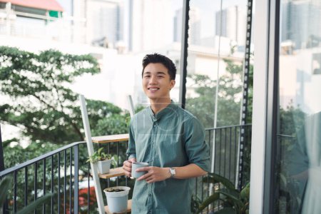 Foto de Hombre feliz contemplando vistas con taza de café en un balcón - Imagen libre de derechos