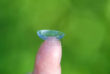 Foto de Lente de contacto transparente en la punta del dedo en verde borroso naturaleza de verano backgroun - Imagen libre de derechos