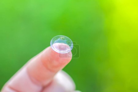 Foto de Lente de contacto transparente en la punta del dedo sobre fondo verde borroso de la naturaleza del verano - Imagen libre de derechos